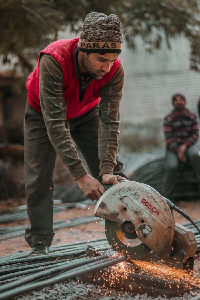 A construction worker in a winter hat using a Bosch electric saw to cut metal outdoors.